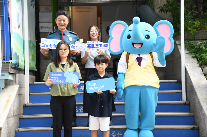 경찰관과 어린이들이 푸른코끼리 마스코트와 함께 계단에서 기념촬영을 하고 있습니다.