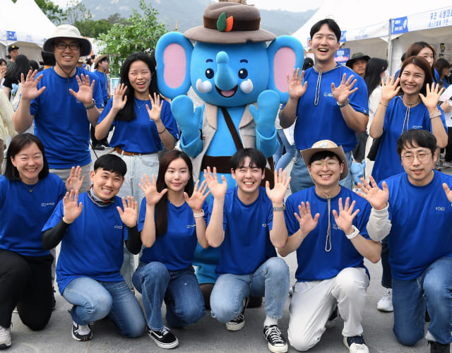 푸른코끼리 행사에서 자원봉사자들이 푸른코끼리 마스코트와 함께 손을 흔들며 사진을 찍고 있습니다.