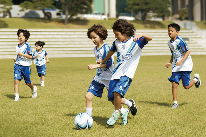 몸 튼튼 클래스에 참가한 다문화 어린이들이 운동장에서 축구를 하고 있습니다.
